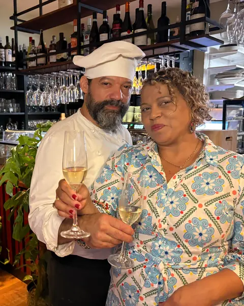 Chef Marcio and Magda raising two glasses of sparkling wine at the bar