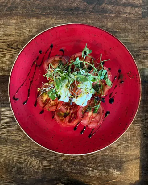Sliced tomatoes, burrata and cress on a red glazed plate